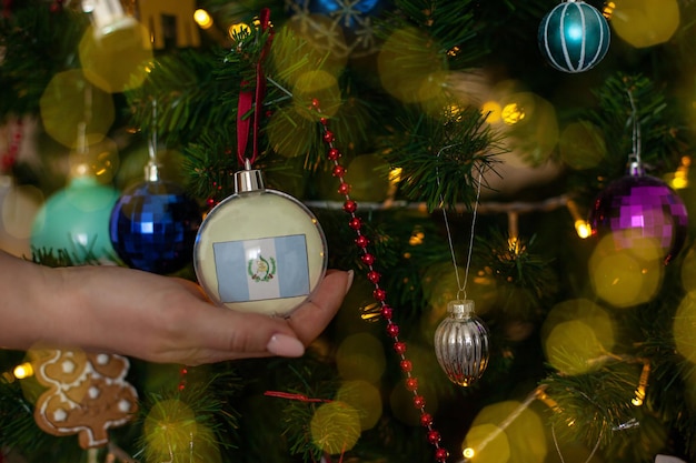 Een meisje houdt een versiering op een kerstboom met de vlag van guatemala