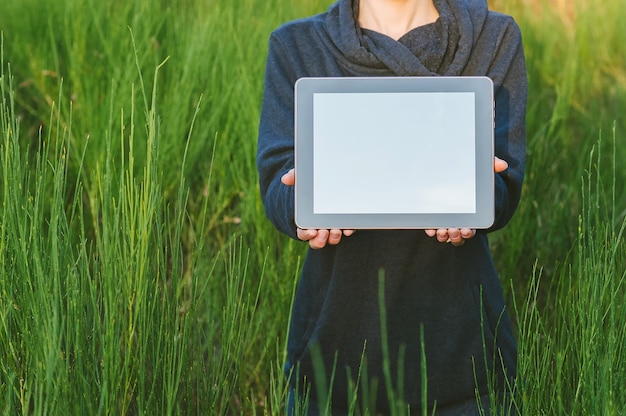 Een meisje in de natuur houdt een tablet in haar handen tegen een achtergrond van prachtig groen.