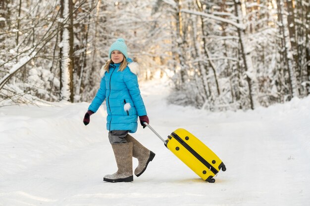 Een meisje in de winter in vilten laarzen gaat met een koffer op een ijzige sneeuwdag