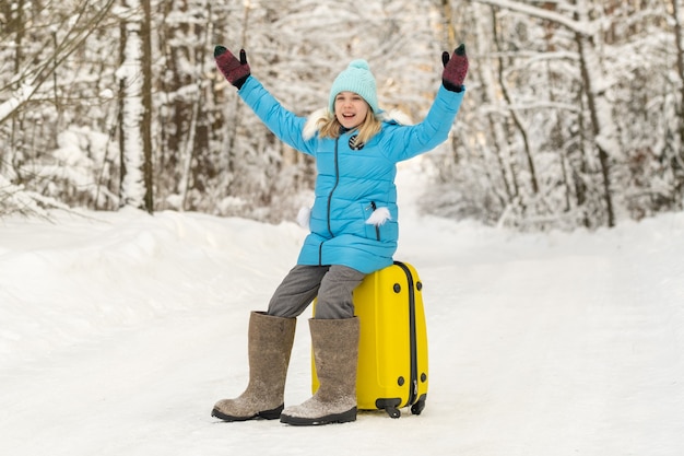 Een meisje in de winter in vilten laarzen zit op een koffer op een ijzige sneeuwdag.