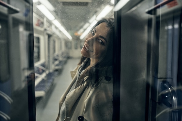 Een meisje in een beige trenchcoat rijdt in een metro.