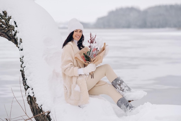 Een meisje in een beige vest met winterbloemen zit in de natuur in een besneeuwd park Winterweer
