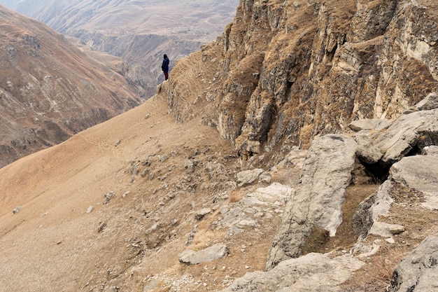 Een meisje in een blauwe jas en bordeauxrode spijkerbroek staat aan de rand van de berg te midden van een zanderige kloof