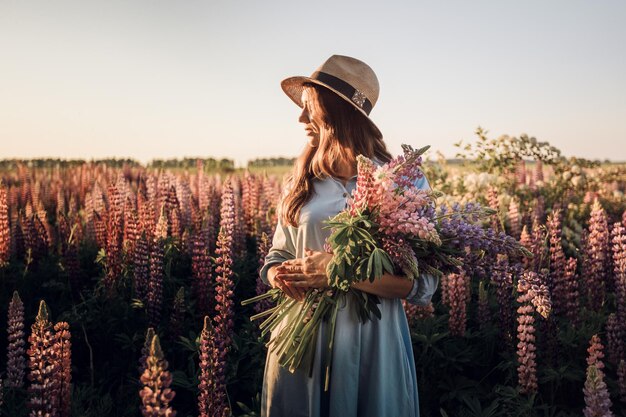 Een meisje in een blauwe jurk op een paars veld met lupines. Weide met paarse bloemen in de zomer.