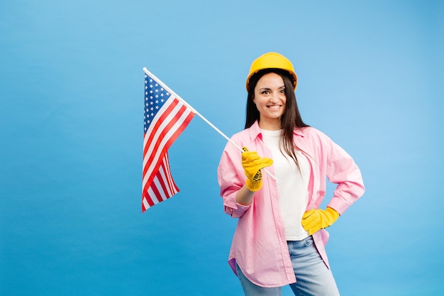 Een meisje in een bouwhelm en handschoenen met een Amerikaanse vlag staat op een blauwe achtergrond