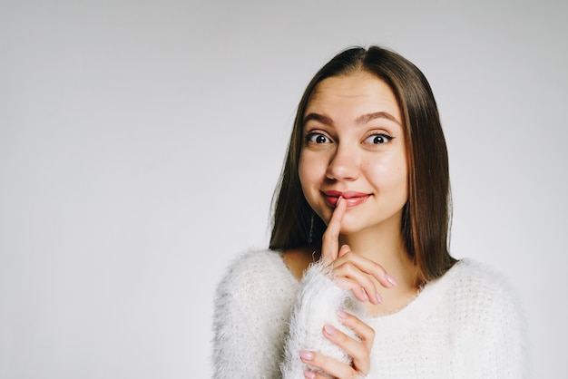 Een meisje in een donzige trui met een glimlach, die haar ogen wijd opende, een vinger op haar lippen legde en om geheimhouding riep