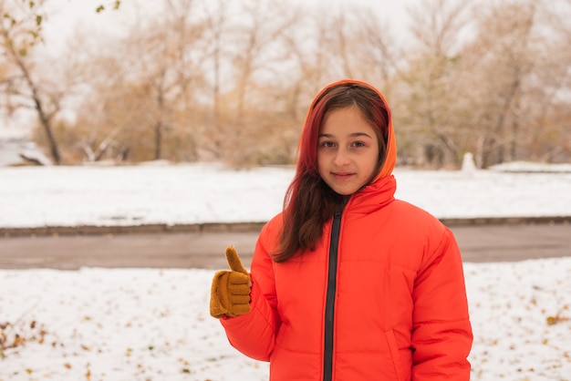 Een meisje in een feloranje warm jasje. Meisje in een oranje jasje bij sneeuwweer. Tienermeisje in de winter