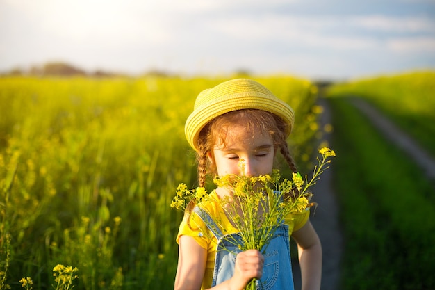 Een meisje in een geel zomerveld ruikt een boeket bloemen. Zonnige dag, vakantie, allergie voor bloei, vrijheid