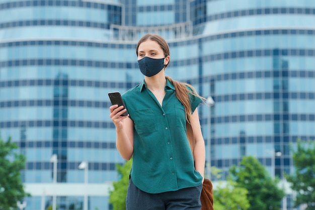 Een meisje in een gezichtsmasker met een smartphone stak een hand in een zak broek in het centrum