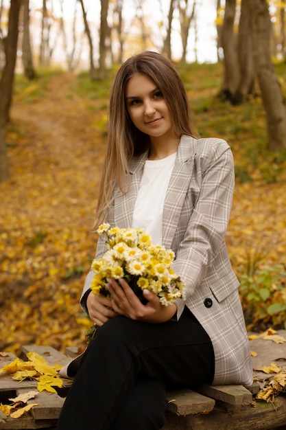 een meisje in een grijze jas op de brug houdt een boeket bloemen vast in het stedelijke herfstbos