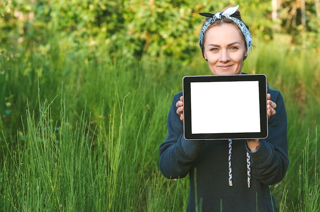 Een meisje in een grijze trui houdt een tabletmodel in haar handen. tegen de achtergrond van prachtige natuur.