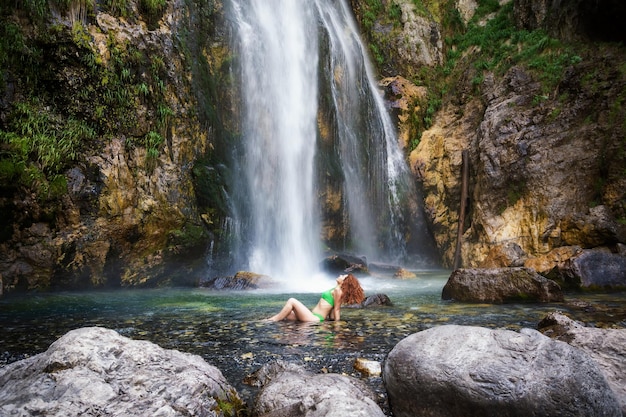 Een meisje in een groen zwempak zit onder de stromen van de waterval Grunas Waterfall is een pittoreske plek in het Nationaal Park Thethi Albanië