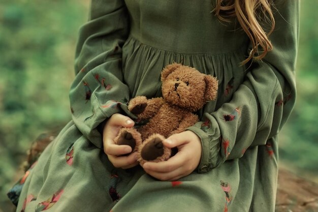 Een meisje in een groene jurk heeft een teddybeer in haar handen Groene lommerrijke achtergrond