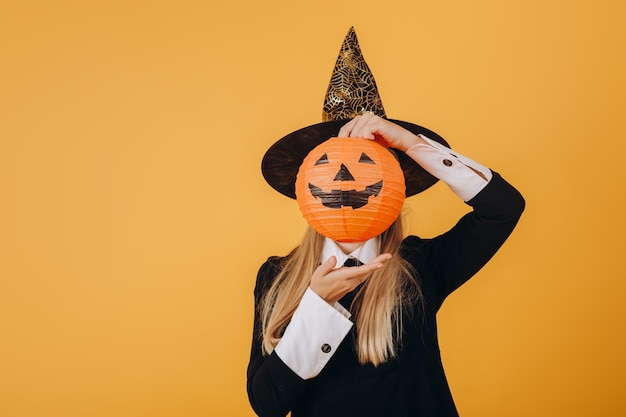 Een meisje in een halloween-kostuum houdt een pompoen rond haar gezicht. Hoge kwaliteit foto