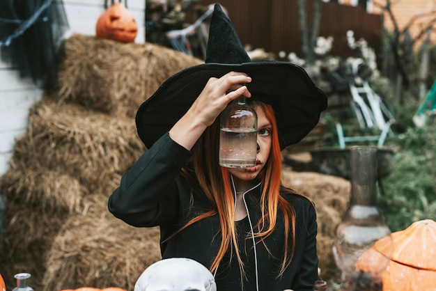 Een meisje in een heksenkostuum kijkt door de glazen lantaarn op de veranda van een huis dat is ingericht om een Halloween-feest te vieren