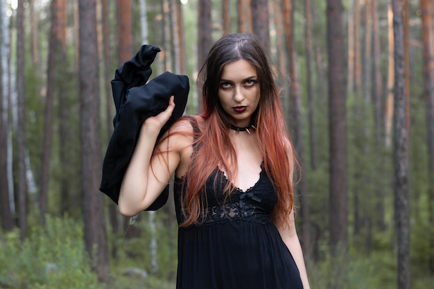 Een meisje in een heksenkostuum met een pentagram om haar nek staat in het bos