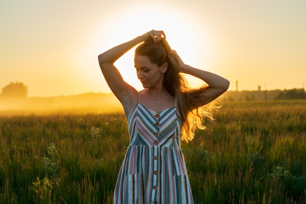 Een meisje in een jurk in een groen veld in de felle stralen van de ondergaande zon.