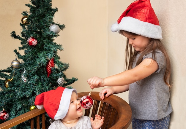 Een meisje in een kerstmuts biedt haar zus een kerstversiering