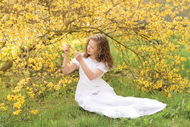 Een meisje in een lange witte jurk in een bloeiende tuin Gele forsythia