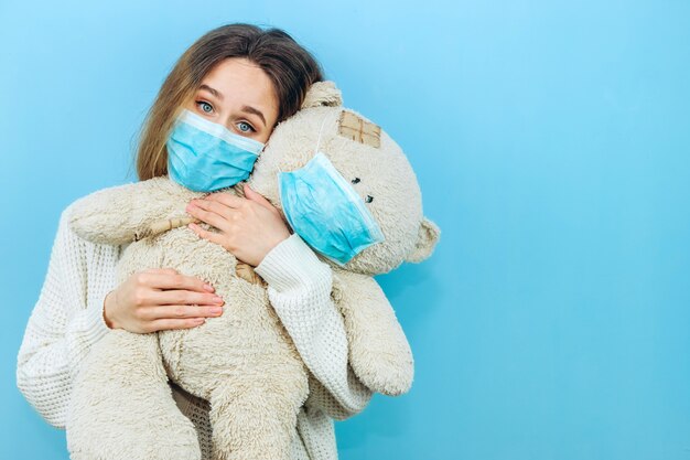 Een meisje in een medisch masker houdt een stuk speelgoed gekleed in een medisch masker op blauw