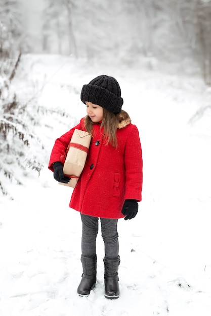 Een meisje in een rode jas staat in het bos met een cadeau