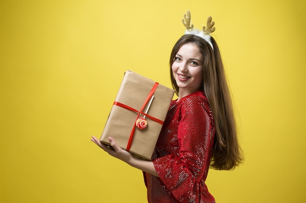 Een meisje in een rode jurk met cadeau tegen een gele achtergrond.