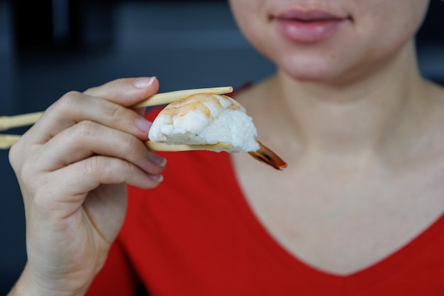 Een meisje in een rode trui houdt sushi vast met gamba's met eetstokjes Zeevruchten