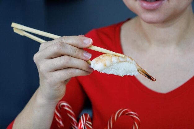 Een meisje in een rode trui houdt sushi vast met gamba's met eetstokjes Zeevruchten