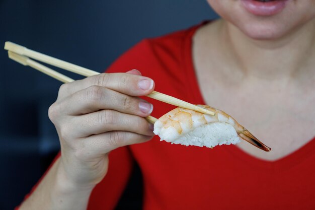 Een meisje in een rode trui houdt sushi vast met gamba's met eetstokjes Zeevruchten