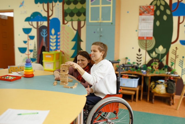 Een meisje in een rolstoel speelt bordspellen aan een tafel Een vrouwelijke psycholoog houdt zich bezig met een gehandicapte