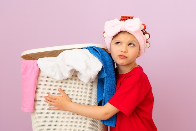 Een meisje in een rood T-shirt houdt een mand met vuile was vast.