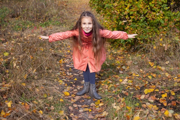 Een meisje in een roze regenjas maakt in de herfst in het park een speelse buiging