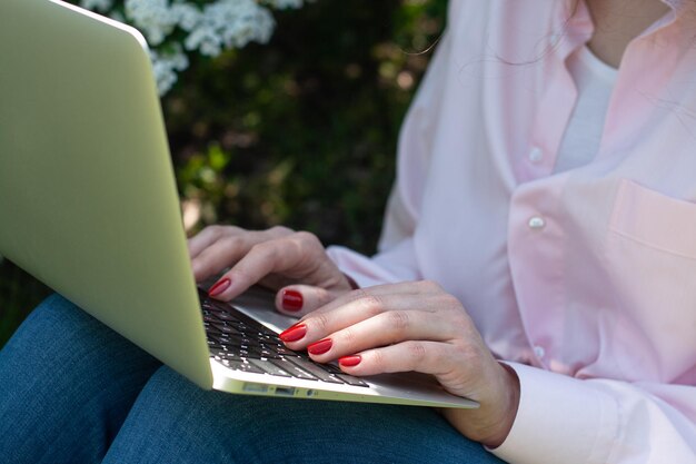 Foto een meisje in een roze shirt zit in de tuin op het gras met een laptophanden met een rode manicure