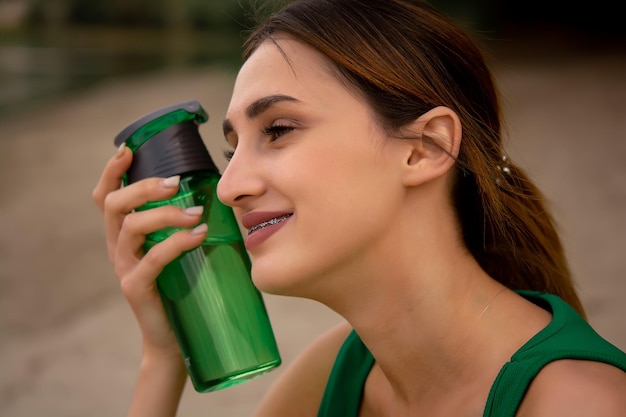 Een meisje in een sportuniform houdt een fles in haar hand een meisje drinkt water uit een fles een meisje is gekleed in een groen trainingspak en een fietsbroek waterbalans buitensporten levensstijl