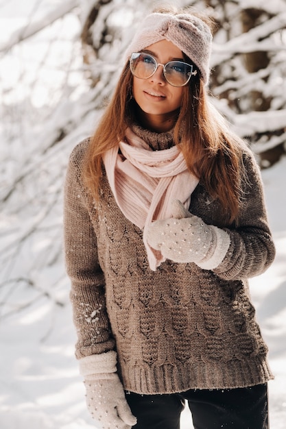 Een meisje in een trui en bril in de winter in een besneeuwd bos.