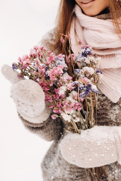 Een meisje in een trui in de winter met een boeket in haar handen staat tussen grote sneeuwbanken