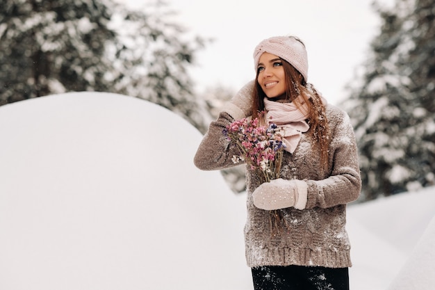 Een meisje in een trui in de winter met een boeket in haar handen staat tussen grote sneeuwbanken.