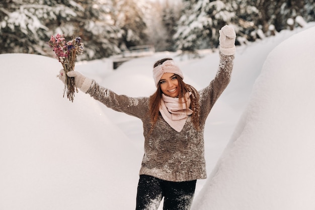 Een meisje in een trui in de winter met een boeket in haar handen staat tussen grote sneeuwbanken