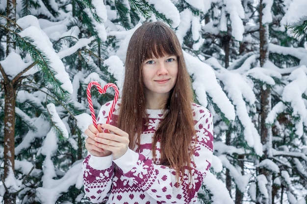 Een meisje in een trui op de achtergrond van met sneeuw bedekte bomen.