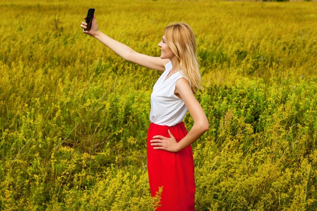 Een meisje in een veld met een zwarte telefoon maakt een selfie. Meisje in het veld met telefoon.