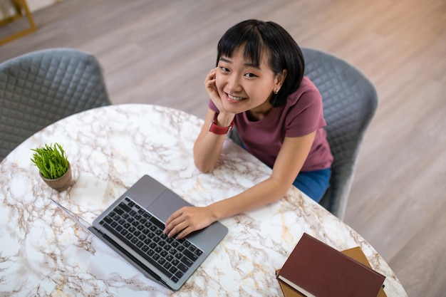 Een meisje in een violet t-shirt dat achter de laptop zit en er gelukkig uitziet