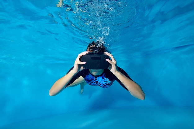 Een meisje in een virtual reality-helm op haar hoofd die onder water zwemt in het zwembad op een blauwe achtergrond