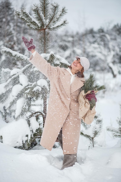 Een meisje in een winterbos met een papieren zak Het meisje schudt de kerstboom waaruit de sneeuw vliegt