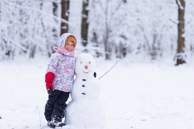 Een meisje in een winterbos staat naast een sneeuwpop