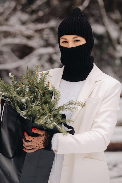 Een meisje in een wit pak en bivakmuts met een pakket kerstbomen in het winterbos op oudejaarsavondNieuwjaarsconcept