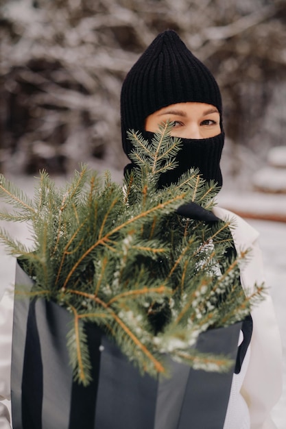 Een meisje in een wit pak en bivakmuts met een pakket kerstbomen in het winterbos op oudejaarsavondNieuwjaarsconcept