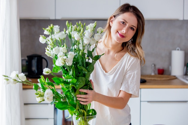 Een meisje in een wit T-shirt maakt een boeket witte rozen klaar voordat ze ze in een vaas op de keukentafel legt. Levensstijl concept