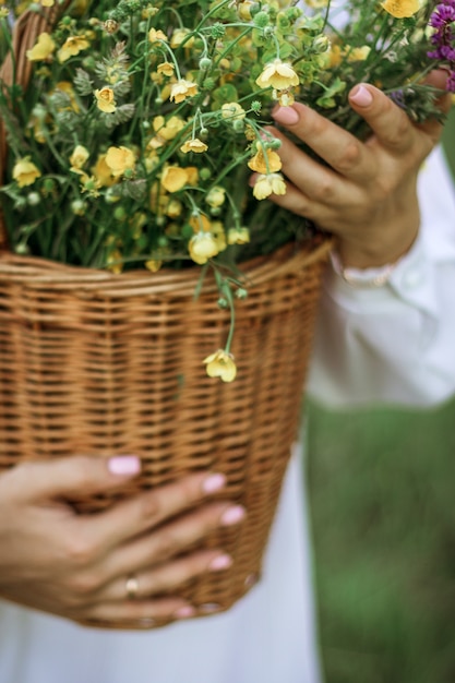 Een meisje in een witte blouse houdt een rieten mand met een boeket wilde bloemen vast. Zomerwandeling in het veld. buik