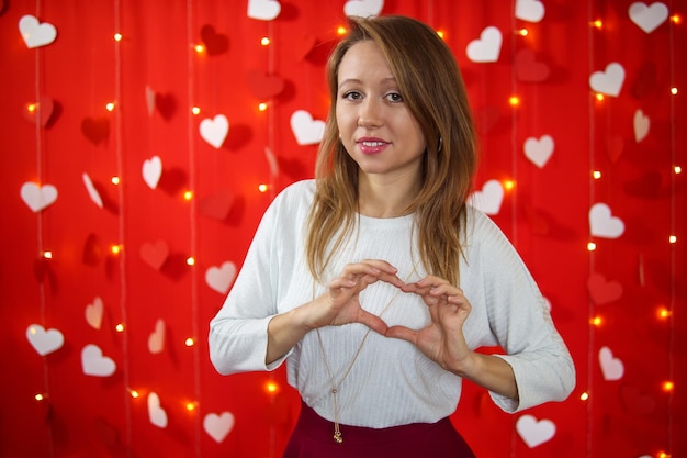 Een meisje in een witte blouse toont een hart met haar handen. Rode achtergrond. Valentijnsdag concept