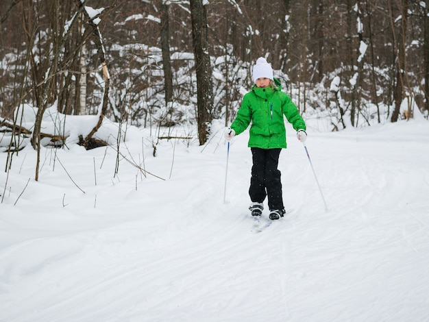 Een meisje in een witte hoed en een groene jas doen oefeningen op ski's.